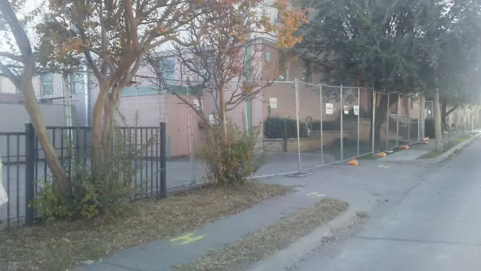 Exterior view of brick treatment facility with metal security fencing, concrete sidewalk, and gated entrance.