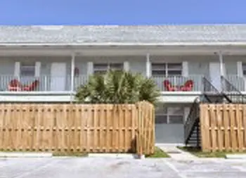 Exterior view of residential building with white walls, wooden deck fencing, railing, and landscaping