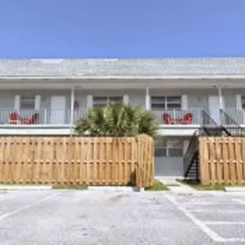 Exterior view of residential building with white walls, wooden deck fencing, railing, and landscaping