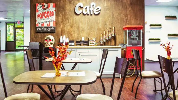Interior cafe space with signage, popcorn machine, coffee counter, seating tables, and decorative wall art