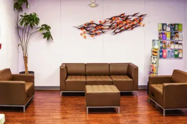 Interior lounge with brown leather seating, decorative artwork, plants, wood flooring, and purple accent walls