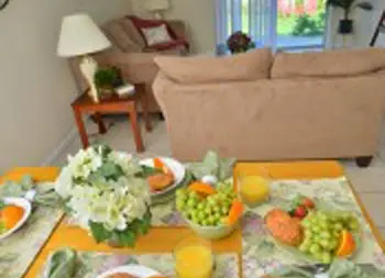 Interior common space showing dining table with fresh produce and beverages, beige sofa, and window access