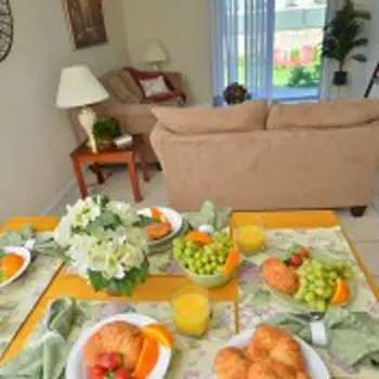 Interior common space showing dining table with fresh produce and beverages, beige sofa, and window access