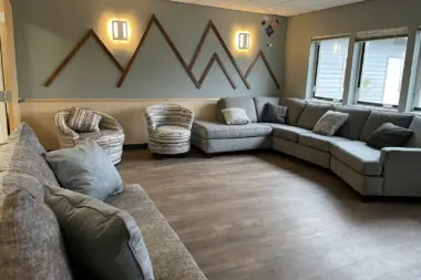Interior common area with sectional sofa, accent chairs, decorative mountain wall art, and natural lighting from windows.
