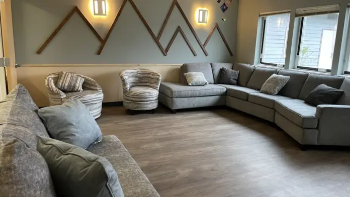 Interior common area with sectional sofa, accent chairs, decorative mountain wall art, and natural lighting from windows.