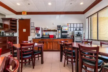 Interior dining space with wooden tables and chairs, coffee station, appliances, and large window with blinds.