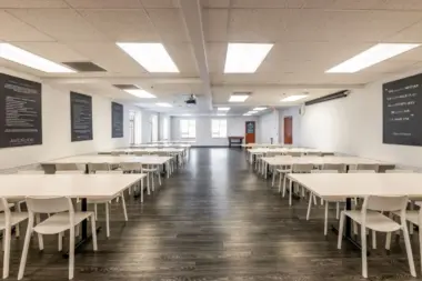 Interior dining room with white tables and chairs, ceiling lighting, and motivational signage on walls