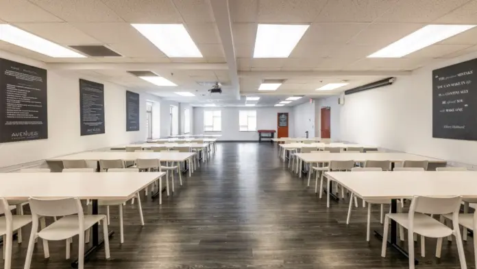 Interior dining room with white tables and chairs, ceiling lighting, and motivational signage on walls