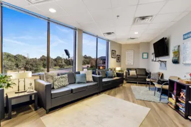Interior lounge area with black couches, entertainment systems, large windows with natural light, and decorative accessories