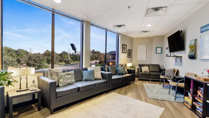 Interior lounge area with black couches, entertainment systems, large windows with natural light, and decorative accessories