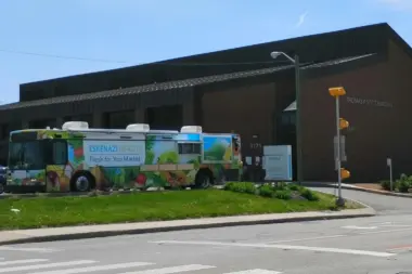 Exterior view showing Eskenazi Health Fresh for You Market mobile unit parked at facility entrance with brick building and street access