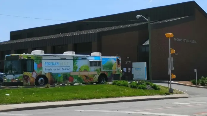 Exterior view showing Eskenazi Health Fresh for You Market mobile unit parked at facility entrance with brick building and street access