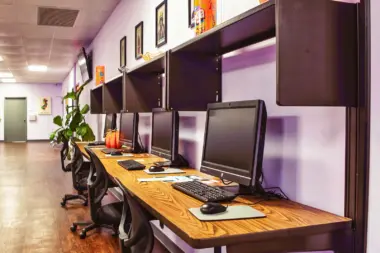 Interior workstation room with purple walls, wooden desks, desktop computers with monitors and office chairs