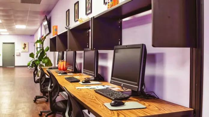 Interior workstation room with purple walls, wooden desks, desktop computers with monitors and office chairs