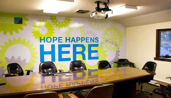 Interior meeting room with conference table, office chairs, ceiling projector, and green gear mural with hope message