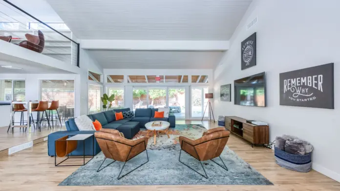 Interior lounge with blue sectional sofa, brown leather chairs, large windows, and modern fireplace
