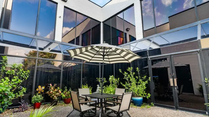 Exterior patio area with striped umbrellas, dining table with chairs, landscaping, and facility building visible in background