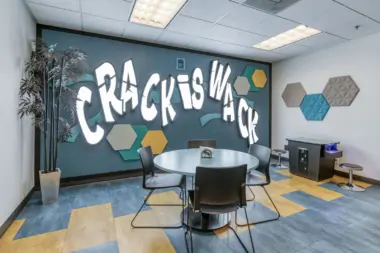 Interior meeting room with round table, chairs, turquoise accent wall with white text graphics, and hexagonal wall tiles