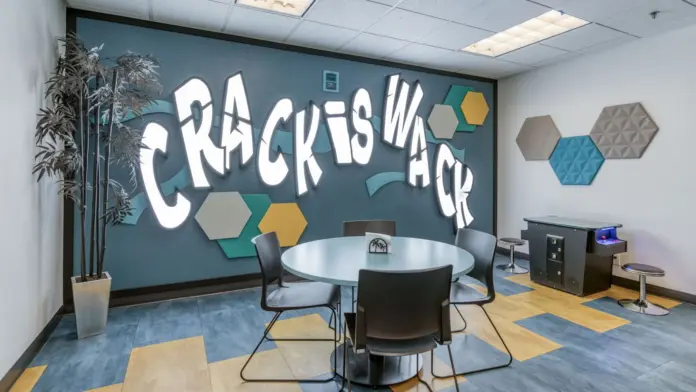 Interior meeting room with round table, chairs, turquoise accent wall with white text graphics, and hexagonal wall tiles