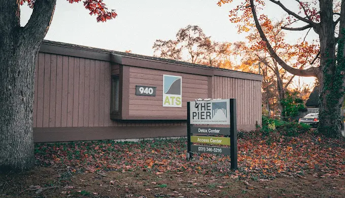 Exterior view of brick building with detox center signage, parking area with vehicles, autumn foliage visible in background