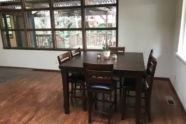 Interior dining room with dark wood table, chairs, hardwood flooring, and large windows overlooking deck