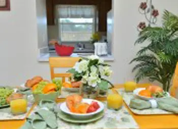 Interior dining area with yellow table, fresh produce and vegetables displayed, window overlooking grounds