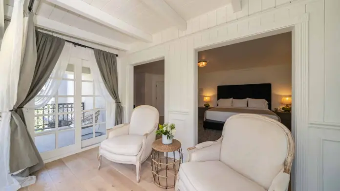 Interior luxury bedroom with upholstered headboard bed, leather seating chair, fireplace, and framed mountain landscape artwork