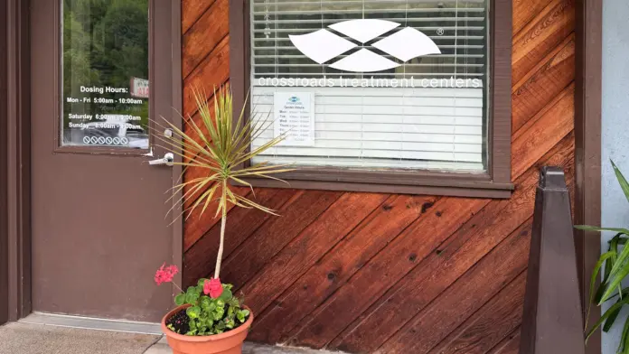 Exterior entrance detail showing brown door with posted dosing hours, window with blinds, and orange flowering plants