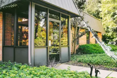 Exterior entrance portico with glass doors, brick facade, metal overhang, and surrounding landscaping