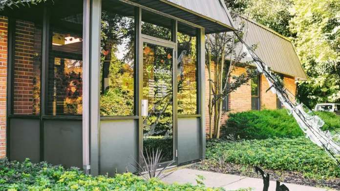 Exterior entrance portico with glass doors, brick facade, metal overhang, and surrounding landscaping