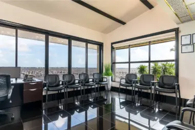 Interior high-rise office with floor-to-ceiling windows, black office chairs, conference tables, and panoramic waterfront cityscape view.