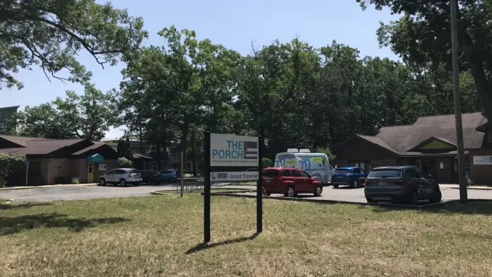Outdoor facility sign mounted on post with campus buildings, parked vehicles, and trees in background