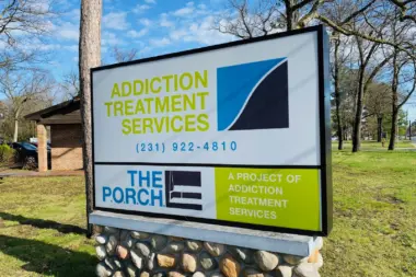 Outdoor ground sign displaying facility name, phone number, and program names in green and blue colors