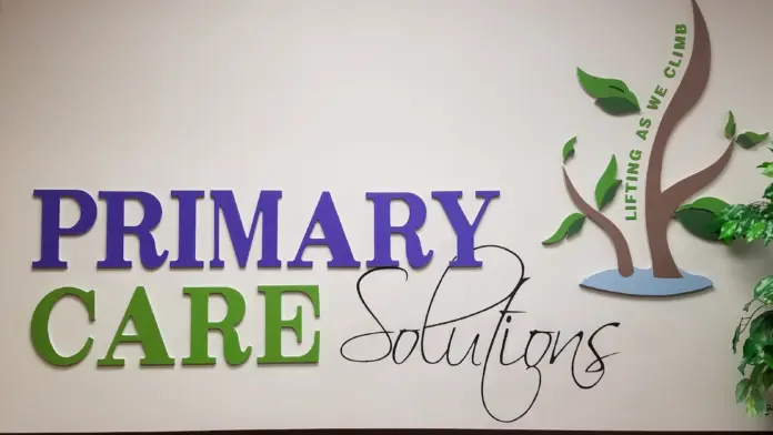 Interior signage showing Primary Care Solutions logo with green and blue tree graphic and tagline on white wall