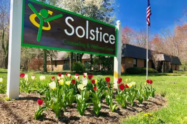 Outdoor ground sign with Solstice logo surrounded by blooming red and white tulips with facility building in background