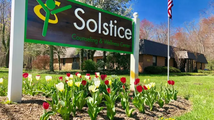 Outdoor ground sign with Solstice logo surrounded by blooming red and white tulips with facility building in background