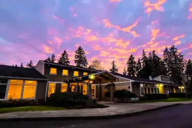 Evening exterior view of modern facility building with lit windows and evergreen trees