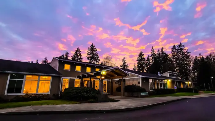 Evening exterior view of modern facility building with lit windows and evergreen trees