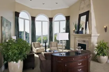 Interior formal living room featuring three large arched windows, fireplace with stone surround, and upholstered furnishings