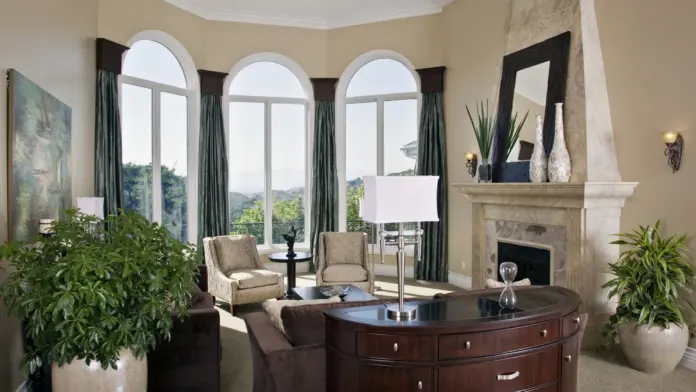 Interior formal living room featuring three large arched windows, fireplace with stone surround, and upholstered furnishings