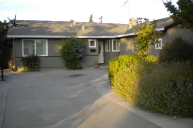 Exterior view of gray residential building with front entrance, driveway, and landscaped shrubs