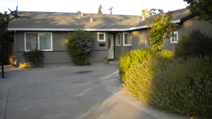 Exterior view of gray residential building with front entrance, driveway, and landscaped shrubs
