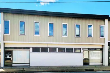 Exterior view of two-story facility with metal siding, upper-level windows, and ground-level storefront entrance with signage
