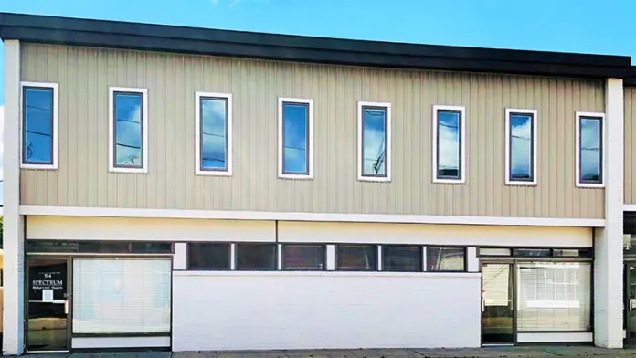 Exterior view of two-story facility with metal siding, upper-level windows, and ground-level storefront entrance with signage
