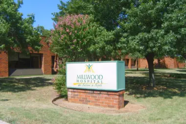 Brick facility building exterior with blooming shrub and tree canopy overlooking manicured grounds