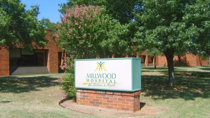 Brick facility building exterior with blooming shrub and tree canopy overlooking manicured grounds