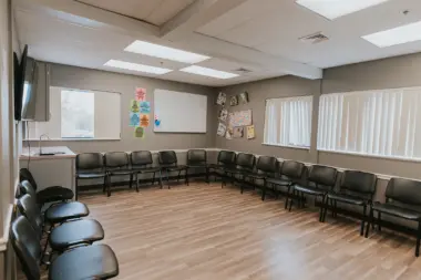 Interior meeting space with curved seating arrangement, black chairs, wooden floors, and windows providing natural light