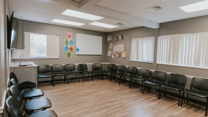 Interior meeting space with curved seating arrangement, black chairs, wooden floors, and windows providing natural light