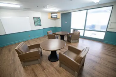 Interior therapy room featuring round tables with brown upholstered chairs, whiteboard, windows, and blue accent wall trim