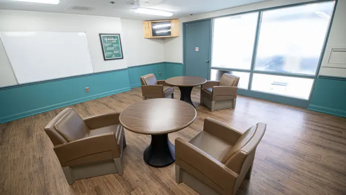 Interior therapy room featuring round tables with brown upholstered chairs, whiteboard, windows, and blue accent wall trim